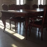 O Comitê Diretor de Bilderberg: Por dentro da estrutura de poder da elite (1954-2024) Sala de conferências elegante, com mesa de madeira ornamentada e cadeiras de couro, iluminação dramática através de um teto alto